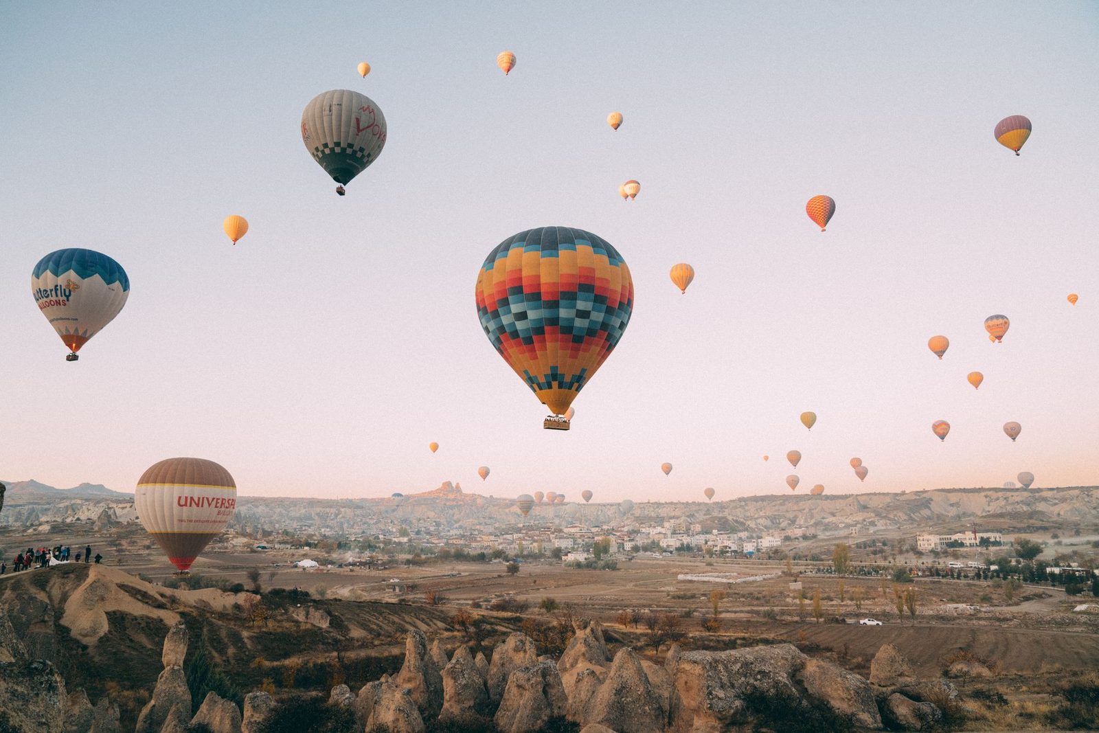 Hot air balloons over the Goreme valley at sunrise, with Uchisar castle in the distance, Cappadocia.