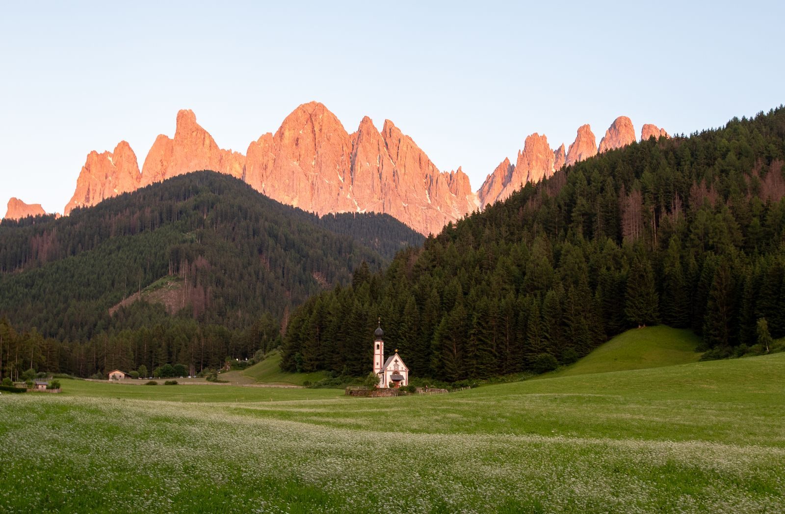 A small church in Val di Funes below the jagged Odle peaks of the Dolomites at sunset.