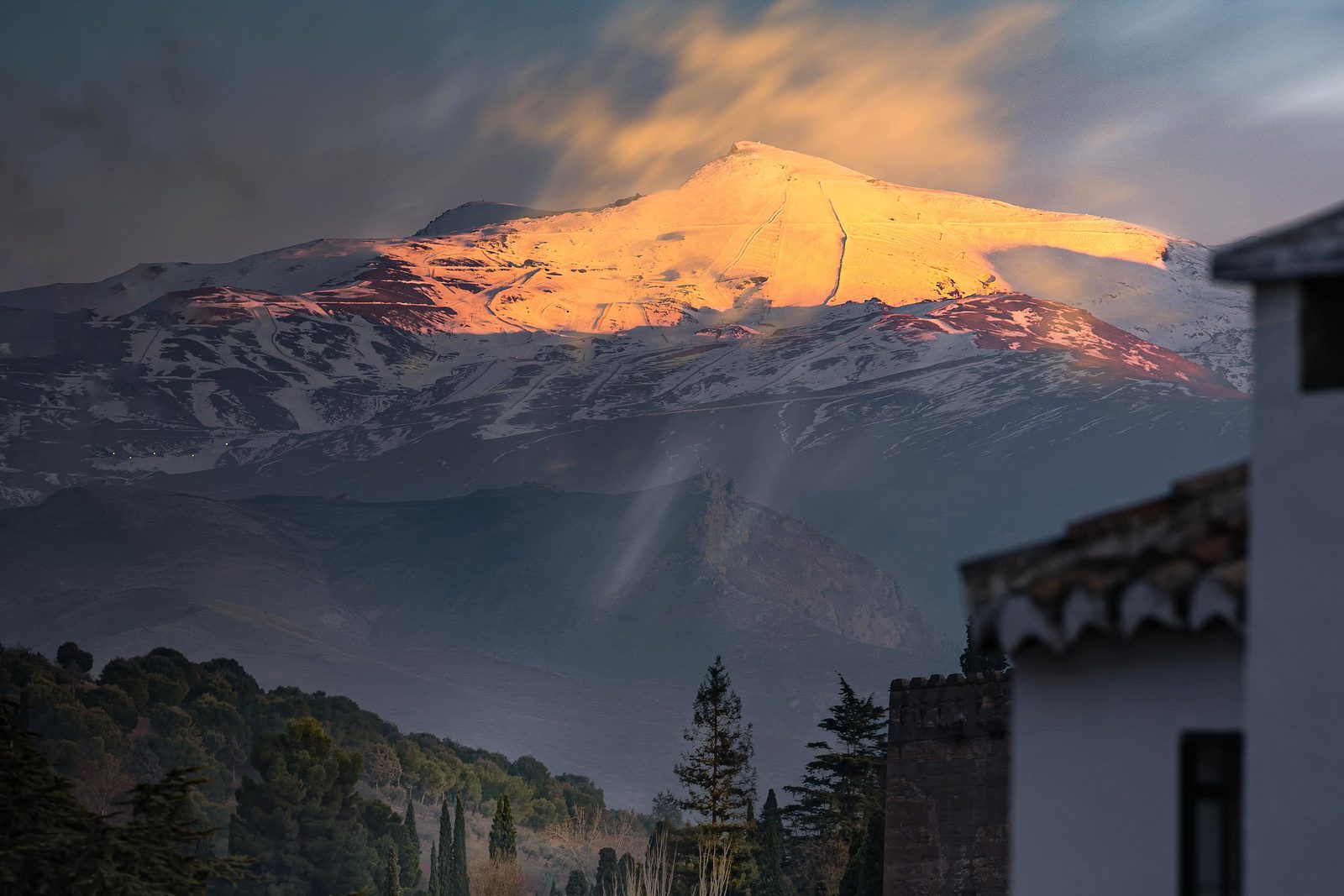 Granada's old quarter and an Alhambra tower below the snow-capped Sierra Nevada at sunset.