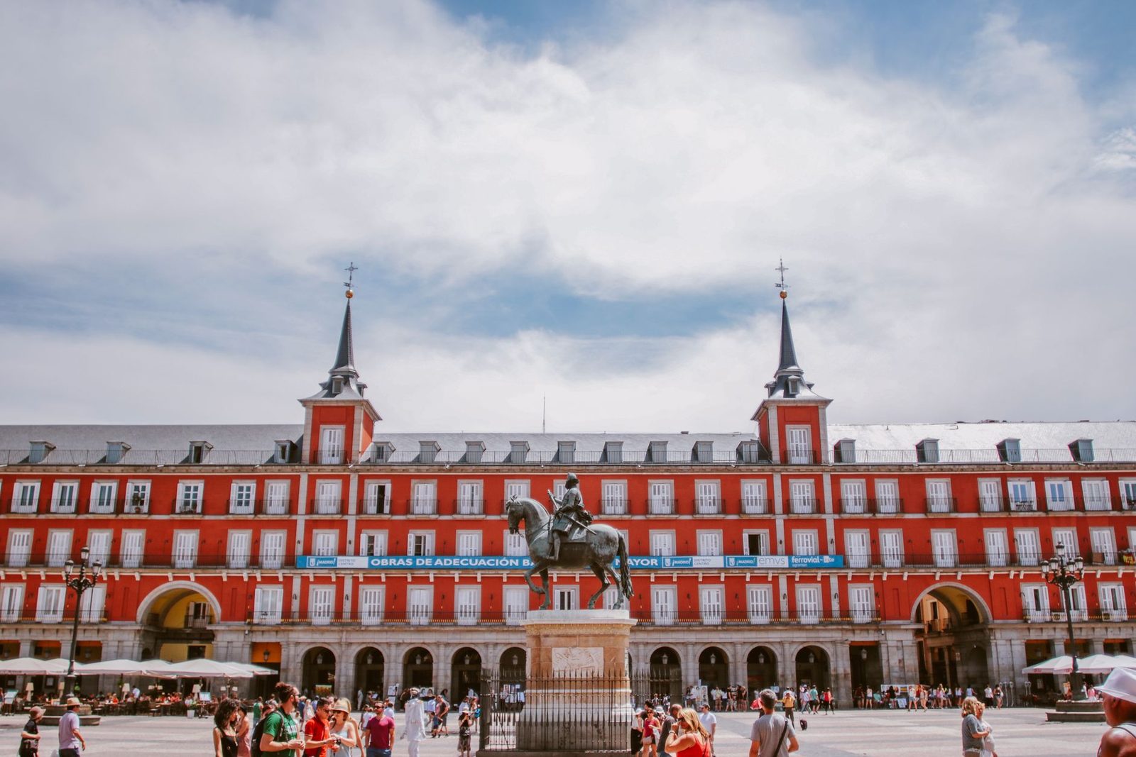 The red facade and equestrian statue of Plaza Mayor in Madrid under a bright sky.
