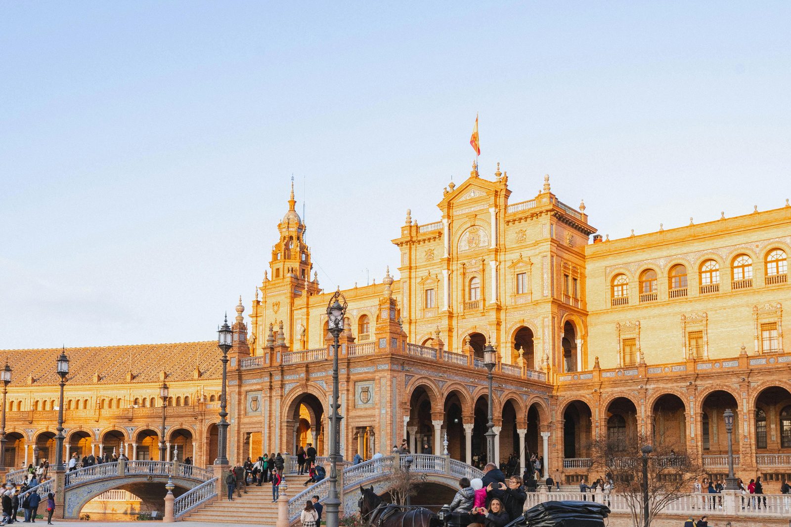 Plaza de Espana in Seville at golden hour, with a horse carriage crossing the tiled square.